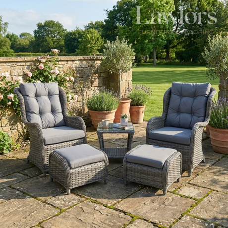 Outdoor patio garden furniture set with gray cushions on a stone patio, surrounded by potted plants and greenery.