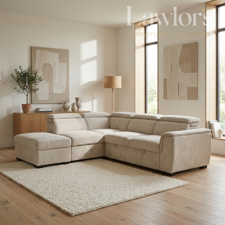 A light beige fabric sectional sofa with a chaise ottoman in a bright, modern living room. The room features light wood floors, a textured cream rug, a wooden sideboard with a potted plant, and large windows with warm natural light.
