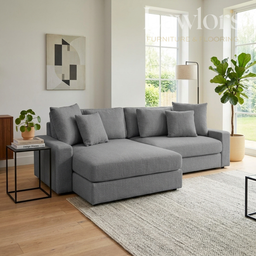 Gray sectional sofa in a living room with a rug, side table, and plant.