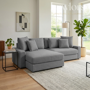 Gray sectional sofa in a living room with a rug, side table, and plant.