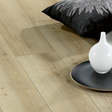 Light oak wood flooring planks shown in a styled room setting with a black decorative pillow and a white vase on a round tray.